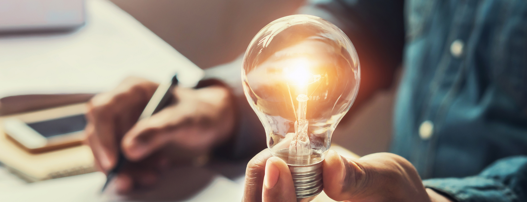 uomo alla scrivania che tiene una lampadina accesa in mano